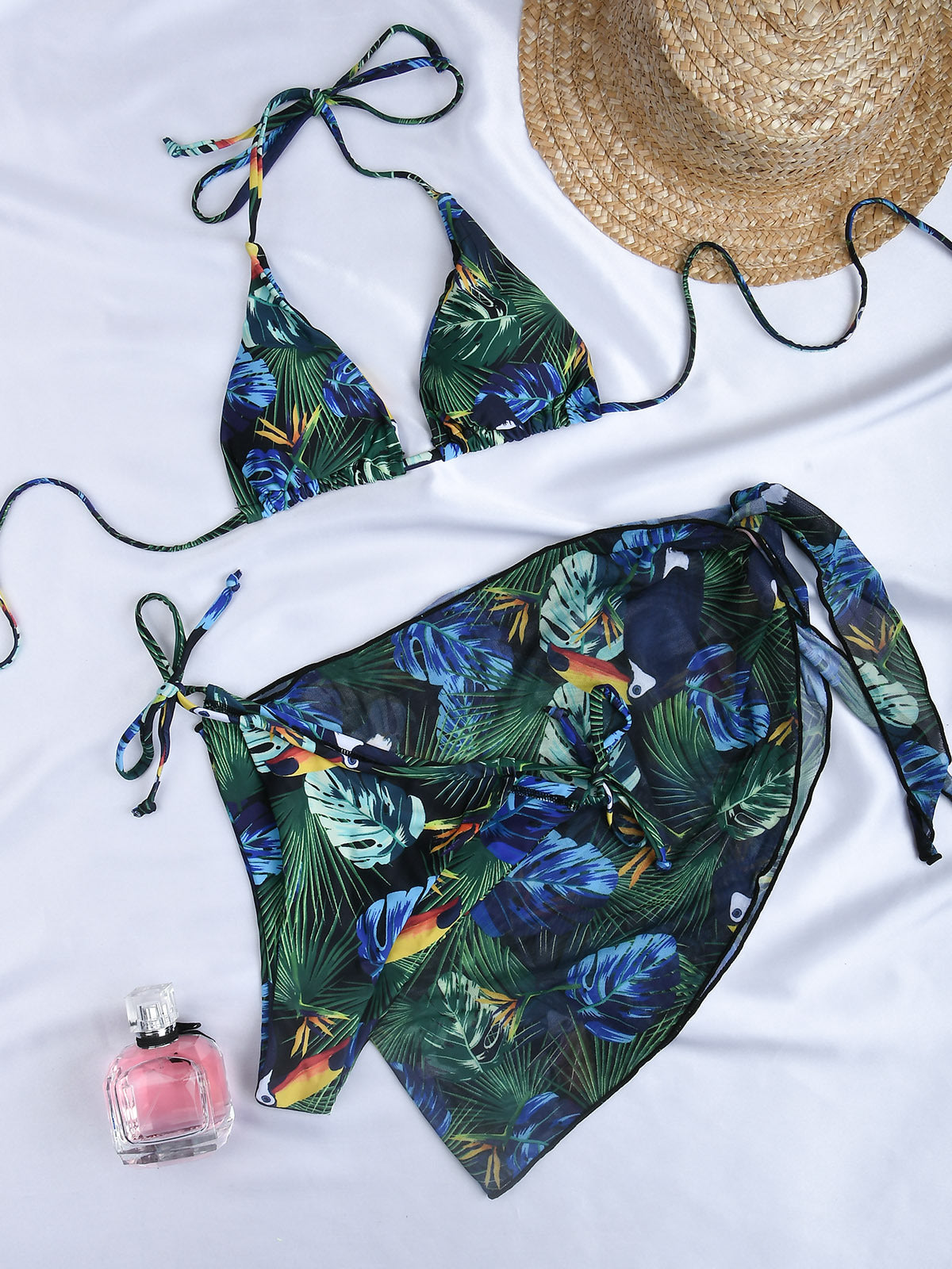 Tropical print bikini set with a straw hat and perfume bottle on a white background.