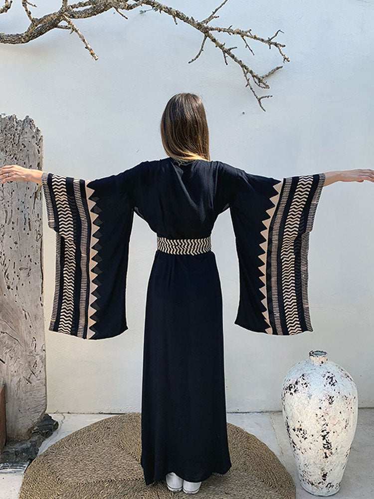 Woman wearing a black dress with patterned sleeves in an outdoor setting.