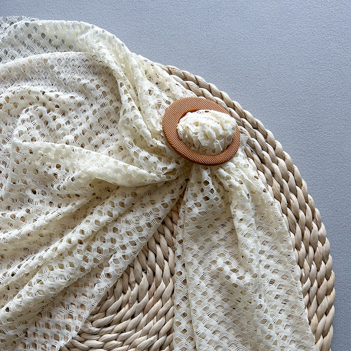Close-up of a woven basket with a lace cover and decorative button on a gray background