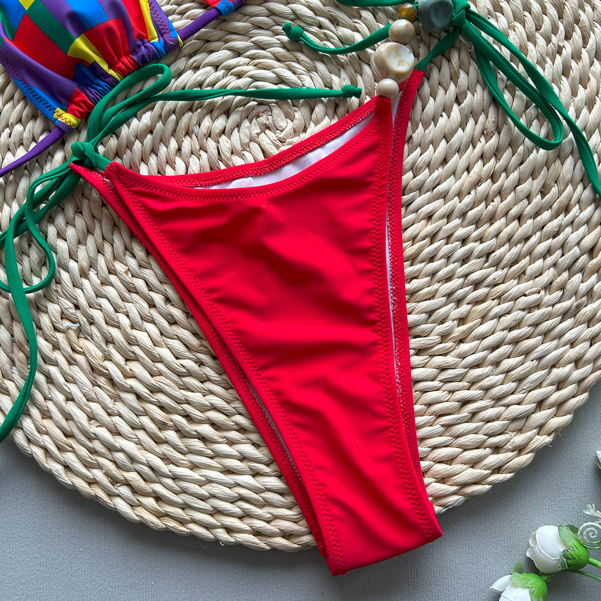 Red bikini bottom on a woven mat with colorful accessories.