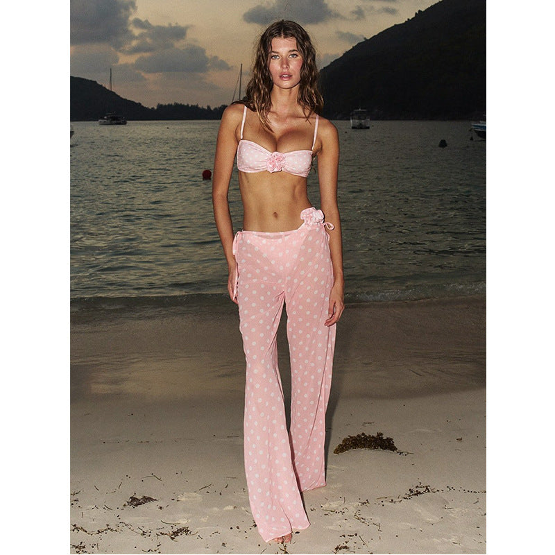 Woman in a pink bikini and polka dot sarong on a beach with sunset and water in the background