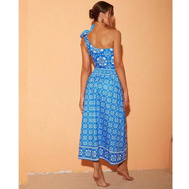 Woman wearing a blue one-shoulder dress with a white pattern against an orange wall.