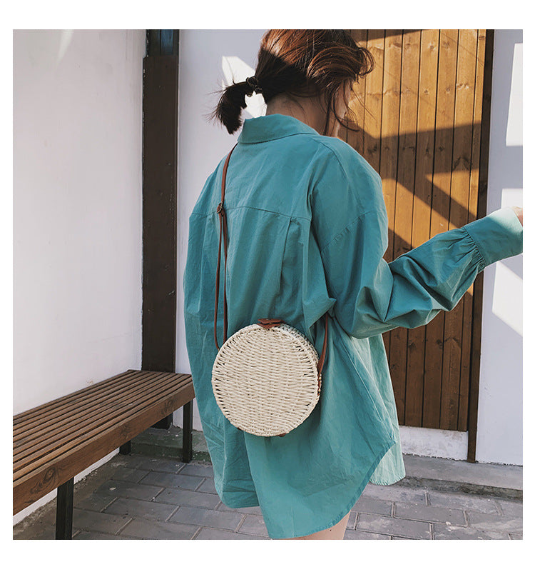 Person wearing a teal shirt with a round woven bag over their shoulder, standing in a sunlit outdoor area.