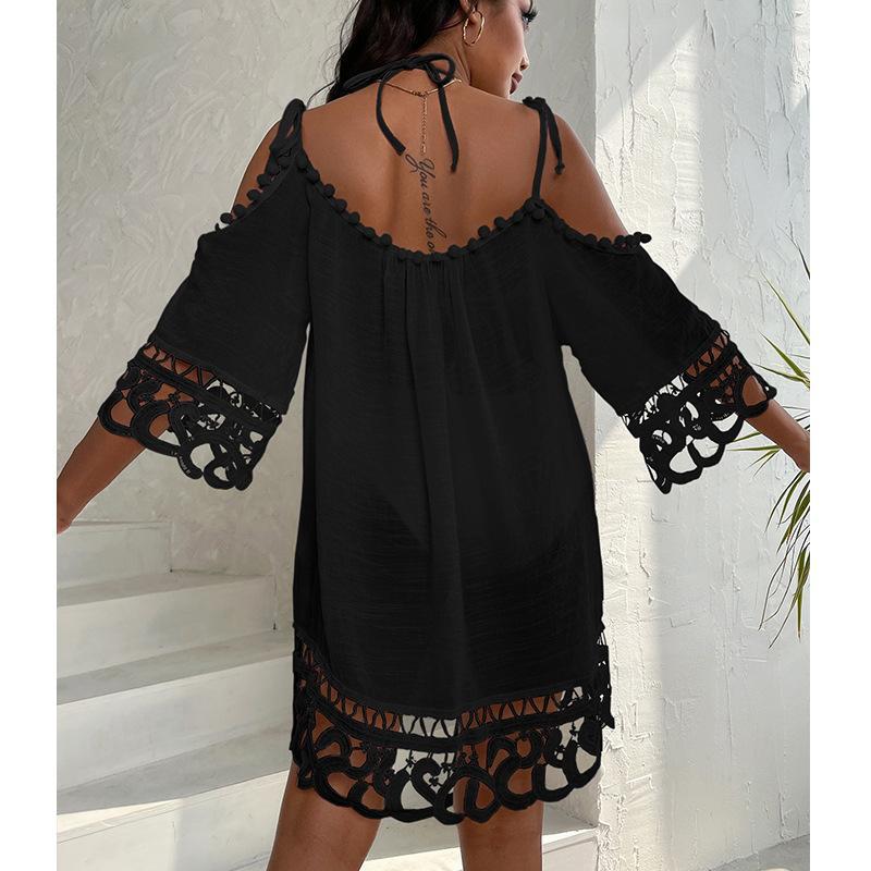 Black off-shoulder dress swimsuit cover-up with lace details worn by a person against a white wall.