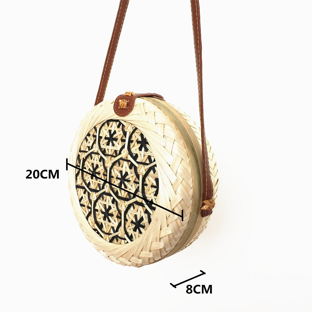 Round woven bag with brown strap and black patterns on a white background