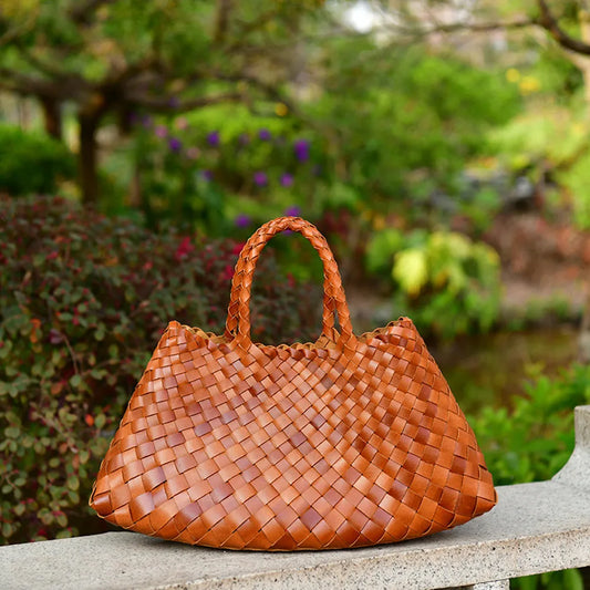Brown woven handbag on a stone ledge with a garden background