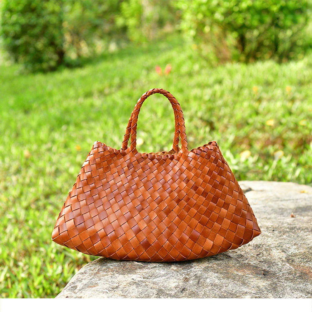 Brown woven handbag on a stone ledge with a garden background