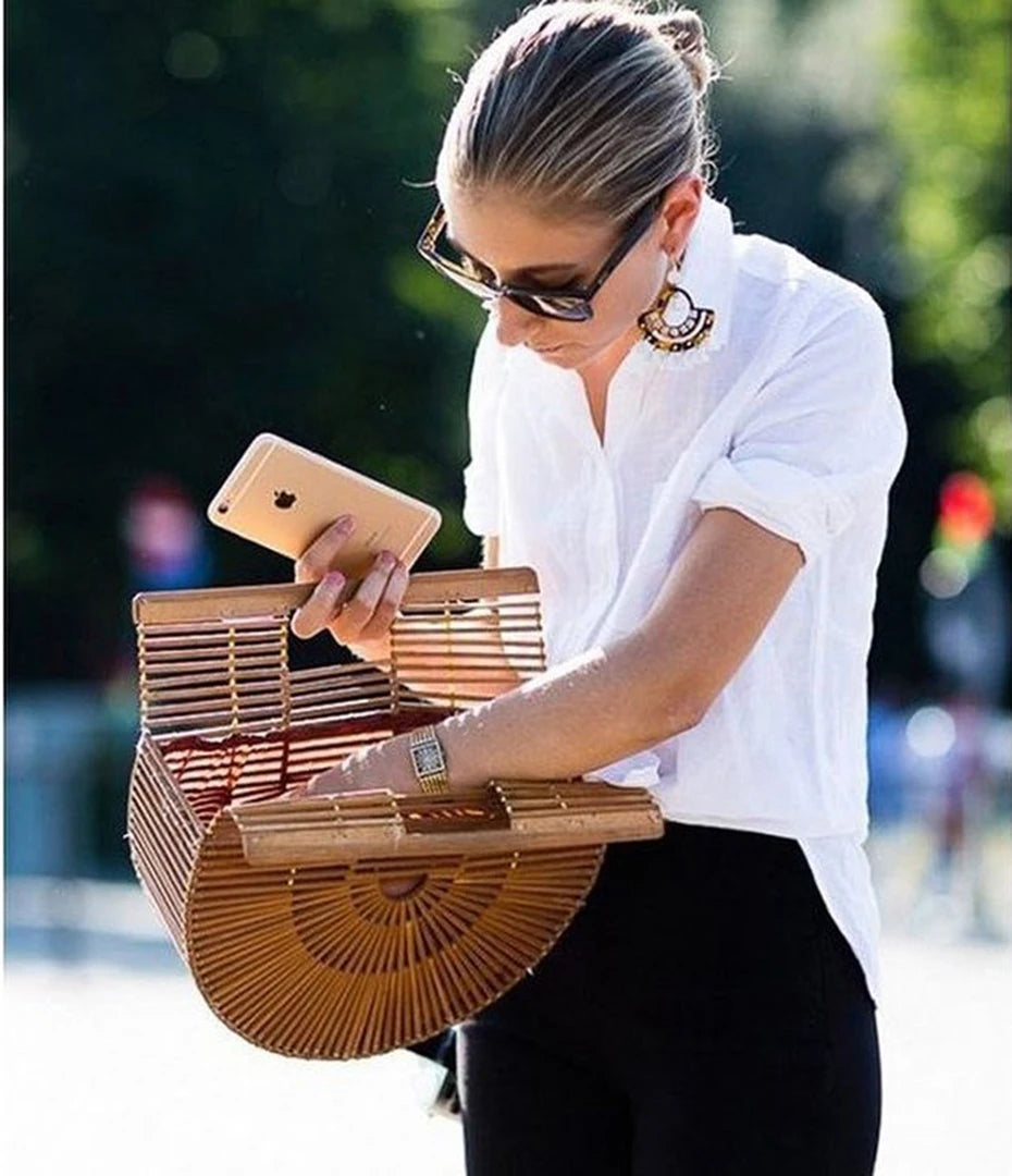 Woman holding a wooden handbag and a phone outdoors
