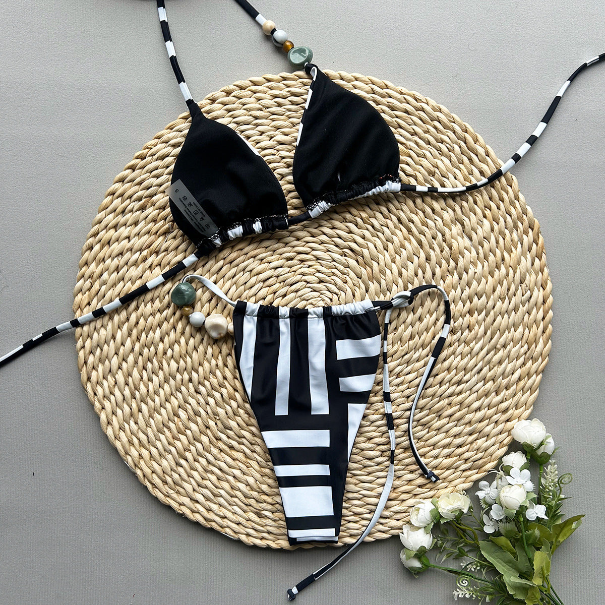 Black and white bikini set on a woven mat with flowers on a gray background