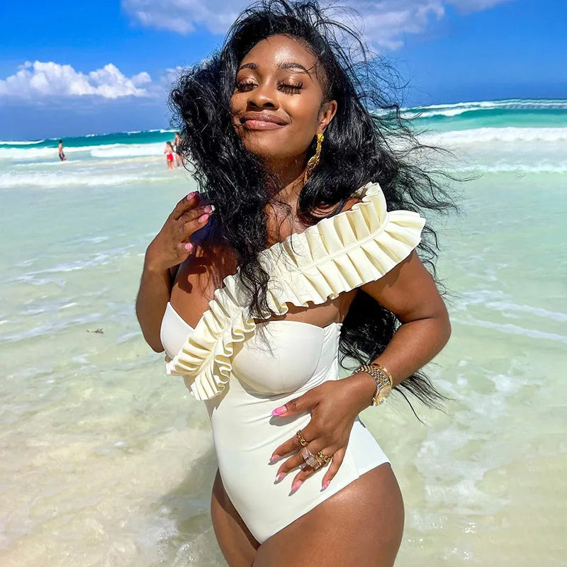 White ruffle backless one‑piece swimsuit with high‑cut leg and ruffle trim, shown against a neutral background.