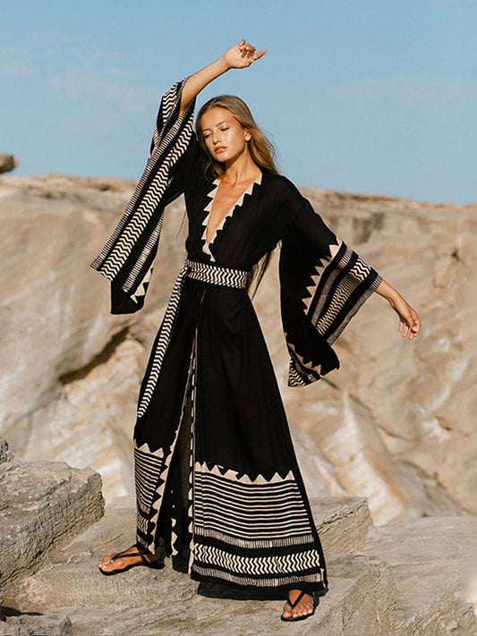 Woman in a black and white patterned dress standing on rocky terrain with a clear sky.