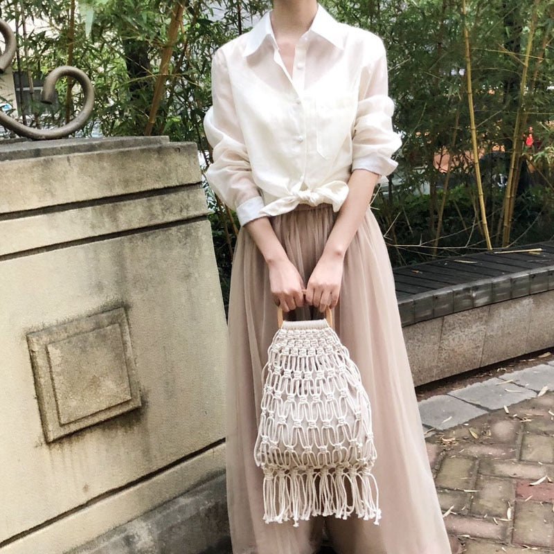 Woman holding a white woven handbag outside.