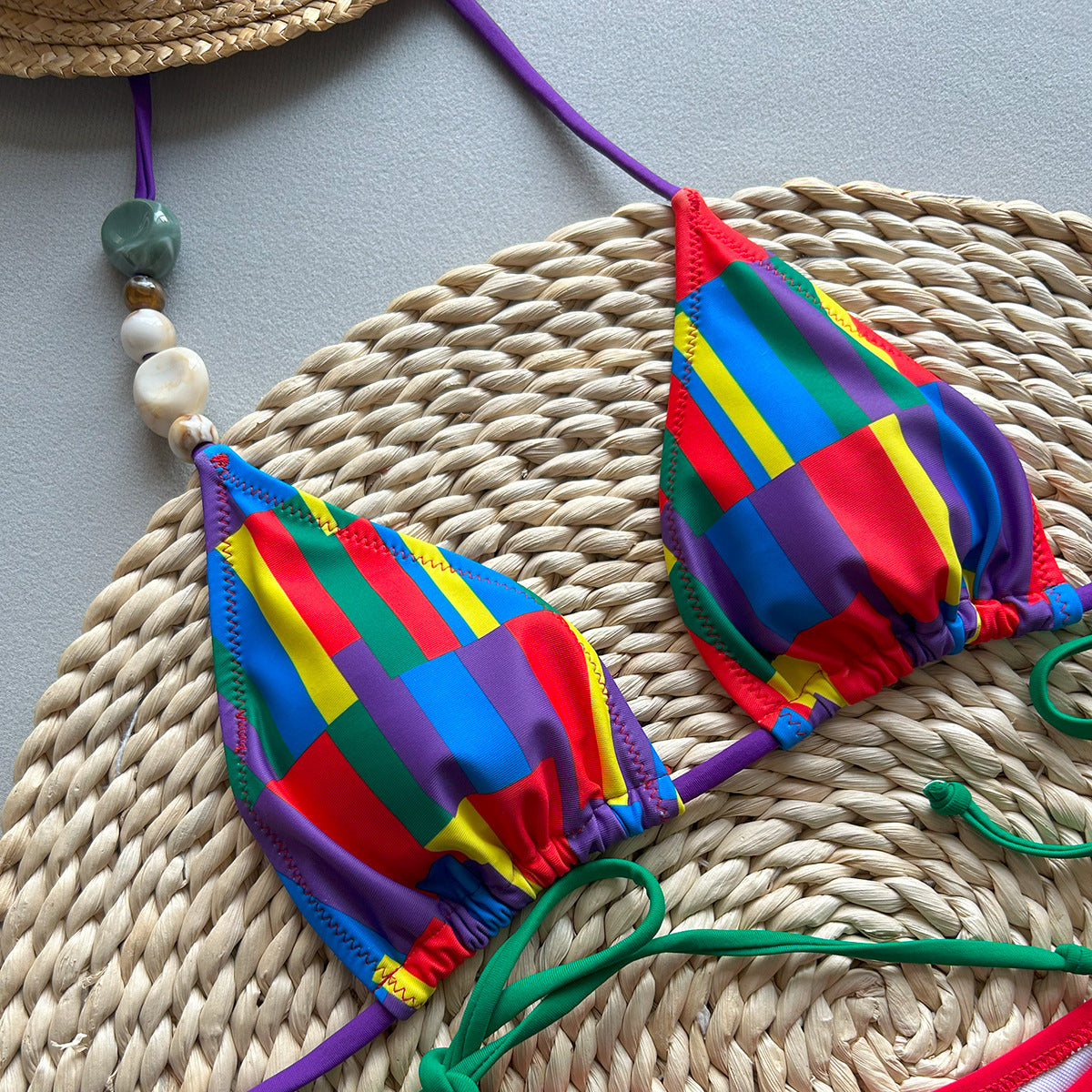 Colorful bikini set on a woven mat with a straw hat and decorative beads in the background.