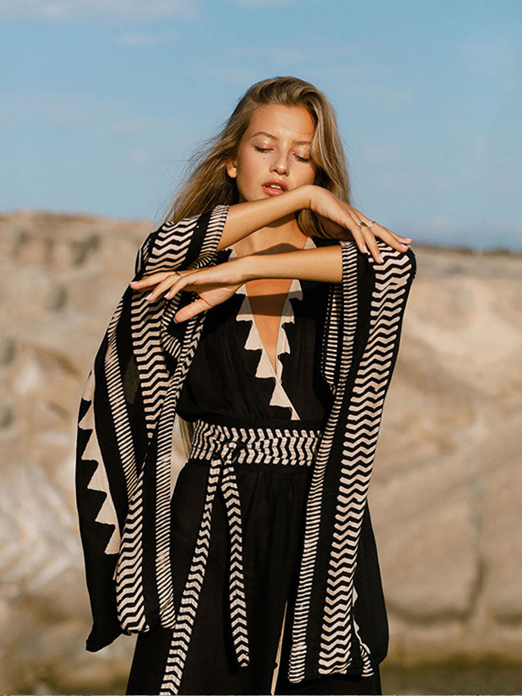 Woman in a black and white patterned dress standing on rocky terrain with a clear sky.