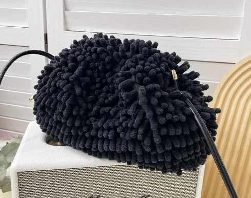 Person holding a black textured handbag against a white wall sold at PeachyBeanz.