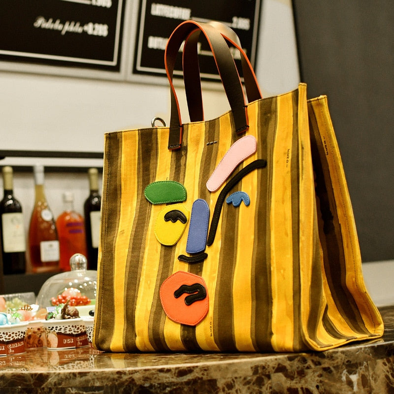 Large yellow striped canvas tote with polyester cotton lining. Modern faceless print, reinforced handles, perfect for beach days and everyday errands.