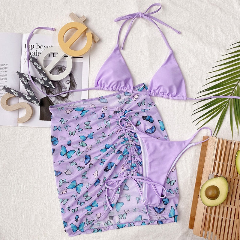 Three‑piece micro bikini set featuring a colorful butterfly print, triangle top with adjustable string ties, matching cheeky bottoms, and a coordinating mini sarong.
