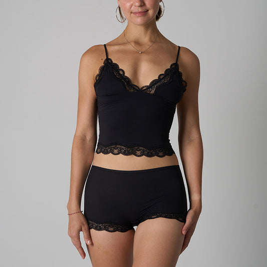 Woman wearing a black lace-trimmed bralette and shorts against a gray background