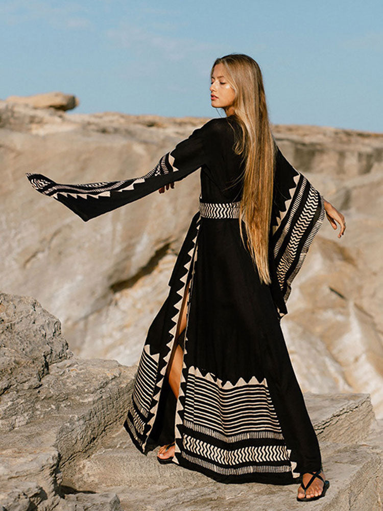 Woman in a black and white patterned dress standing on rocky terrain with a clear sky.