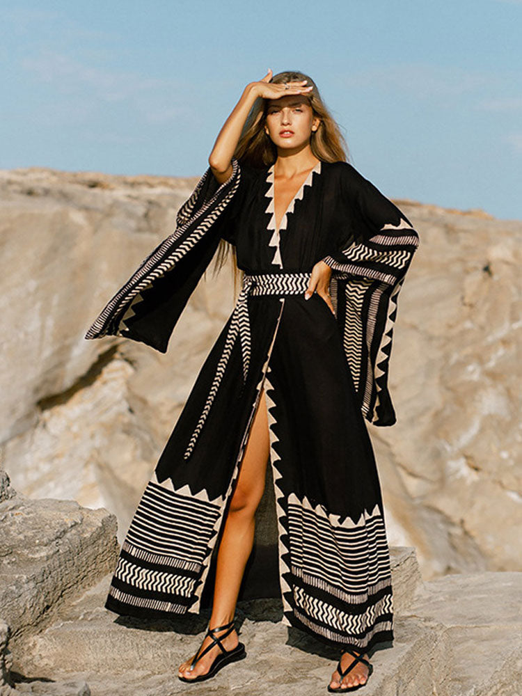 Woman in a black and white patterned dress standing on rocky terrain with a clear sky.