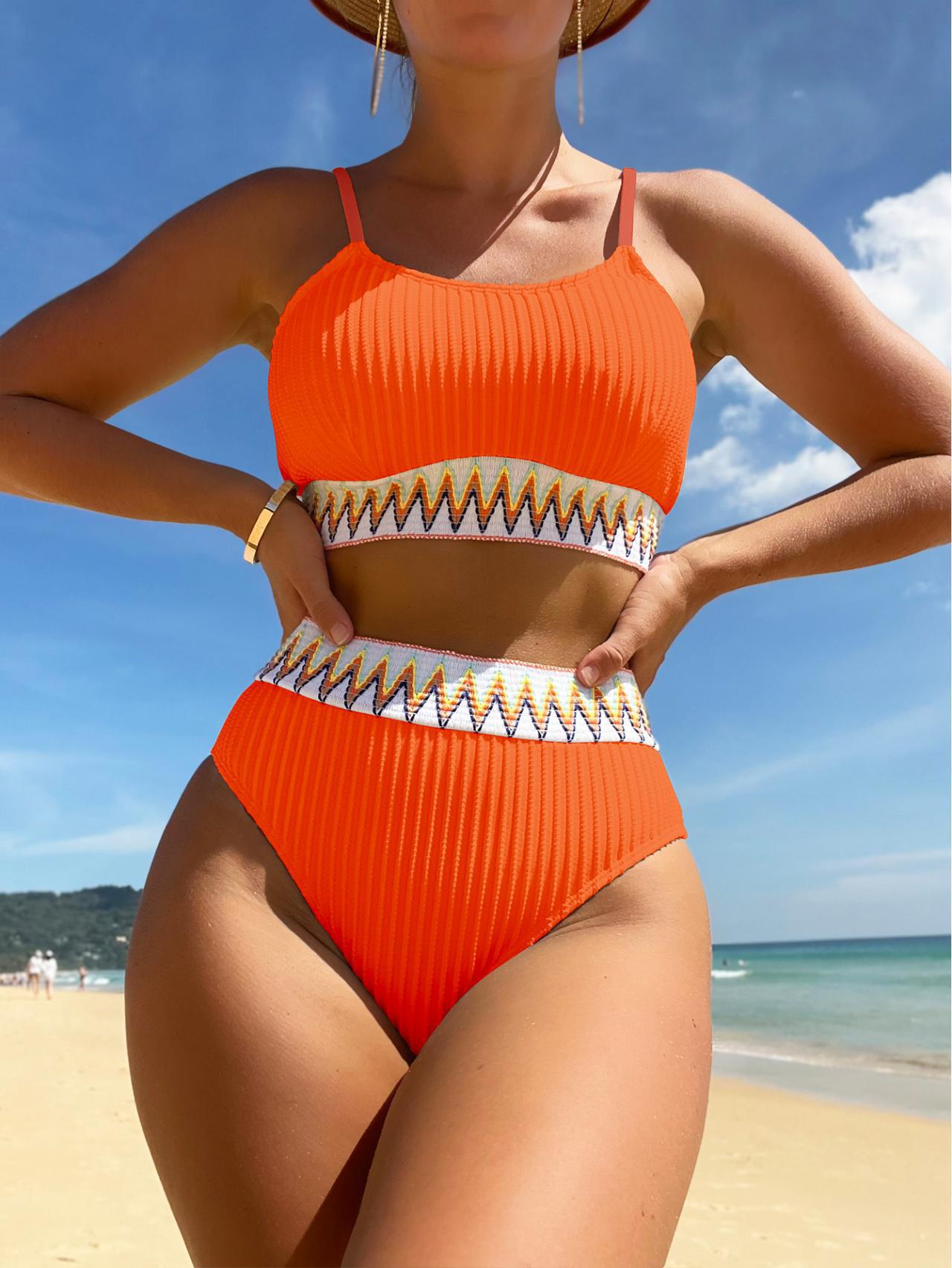 Person wearing a orange bikini with gold accents on a beach
