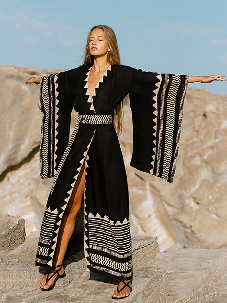 Woman in a black and white patterned dress standing on rocky terrain with a clear sky.