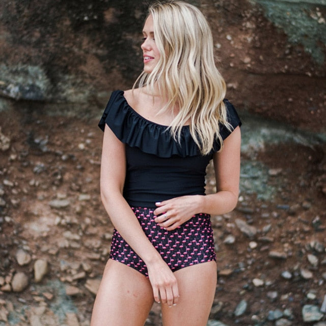 Woman wearing a black top and shorts standing against a rocky background