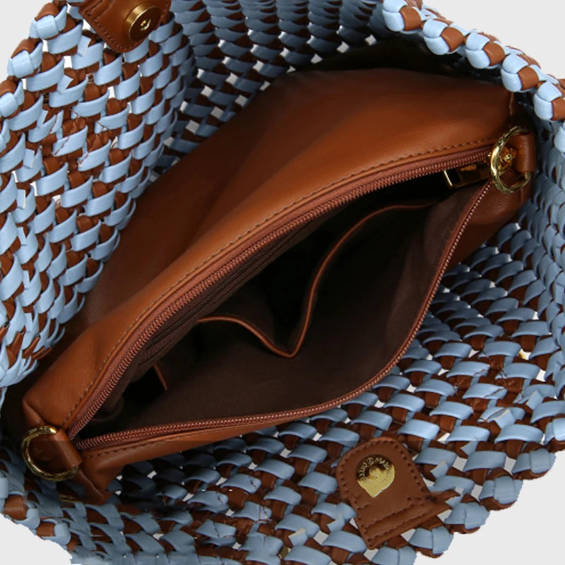 Brown leather bag with gold zipper inside a woven blue and brown bag.