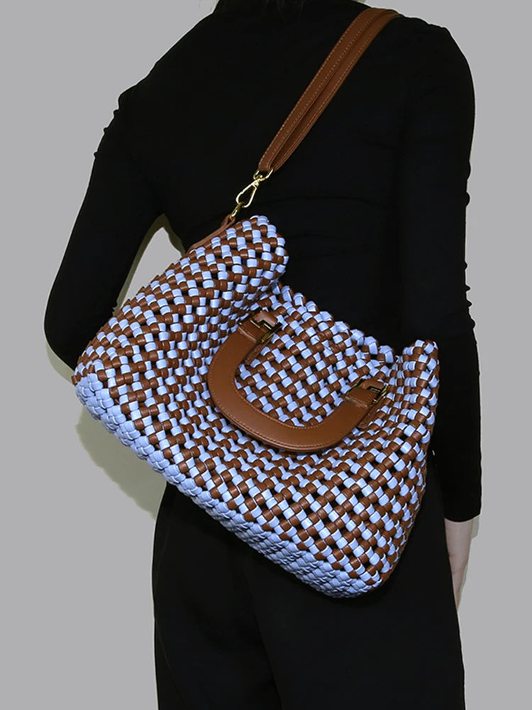 Woven handbag with brown handle and blue body held by a person against a neutral background