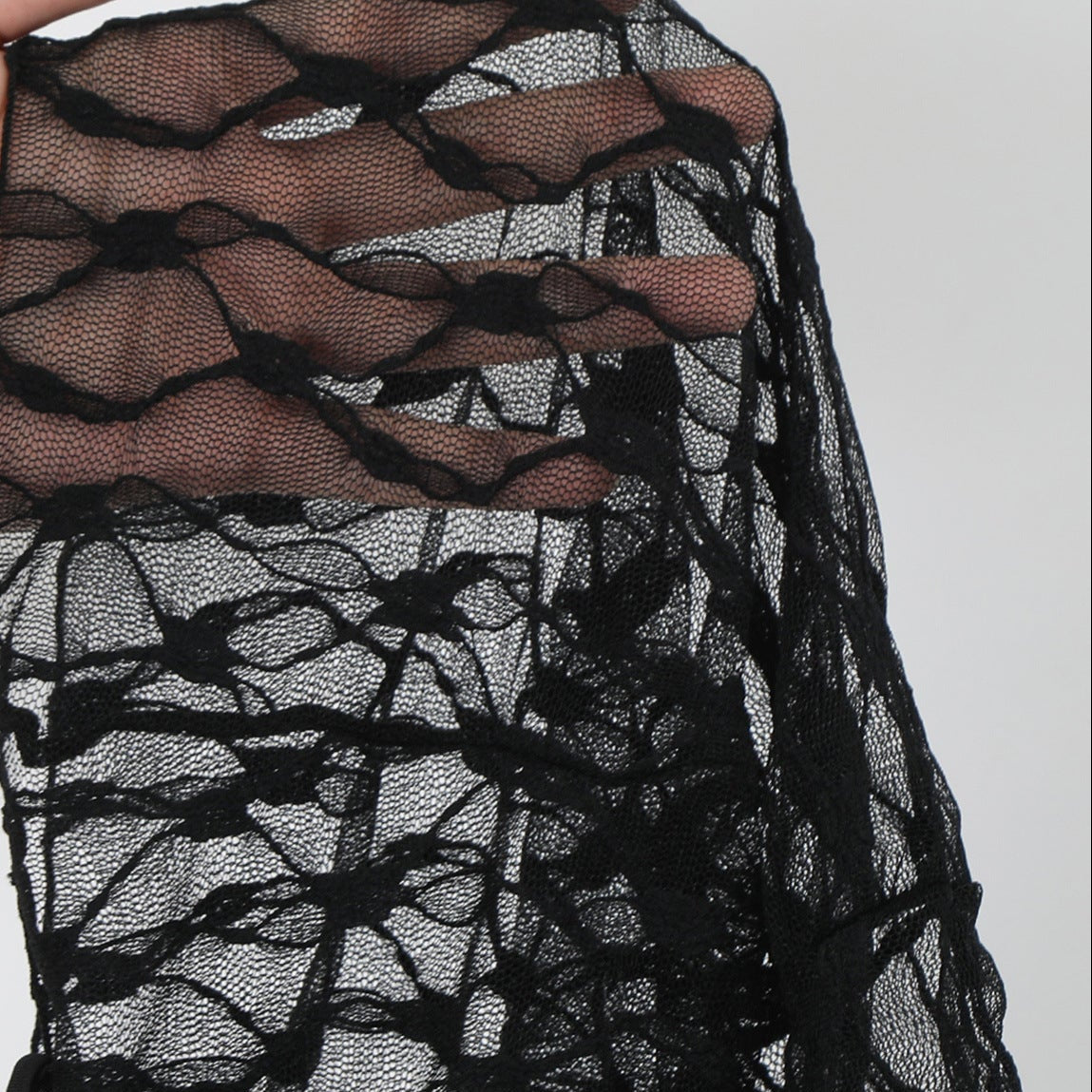 Black lace fabric held by a hand against a white background