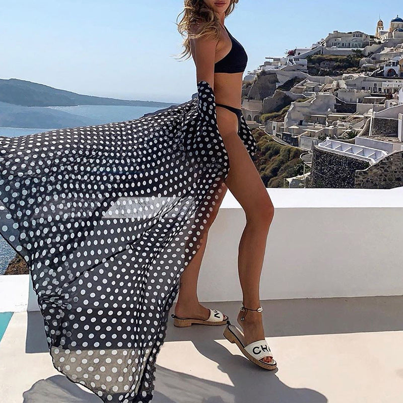 Woman in a black bikini and polka dot cover-up with a scenic view of a coastal town.