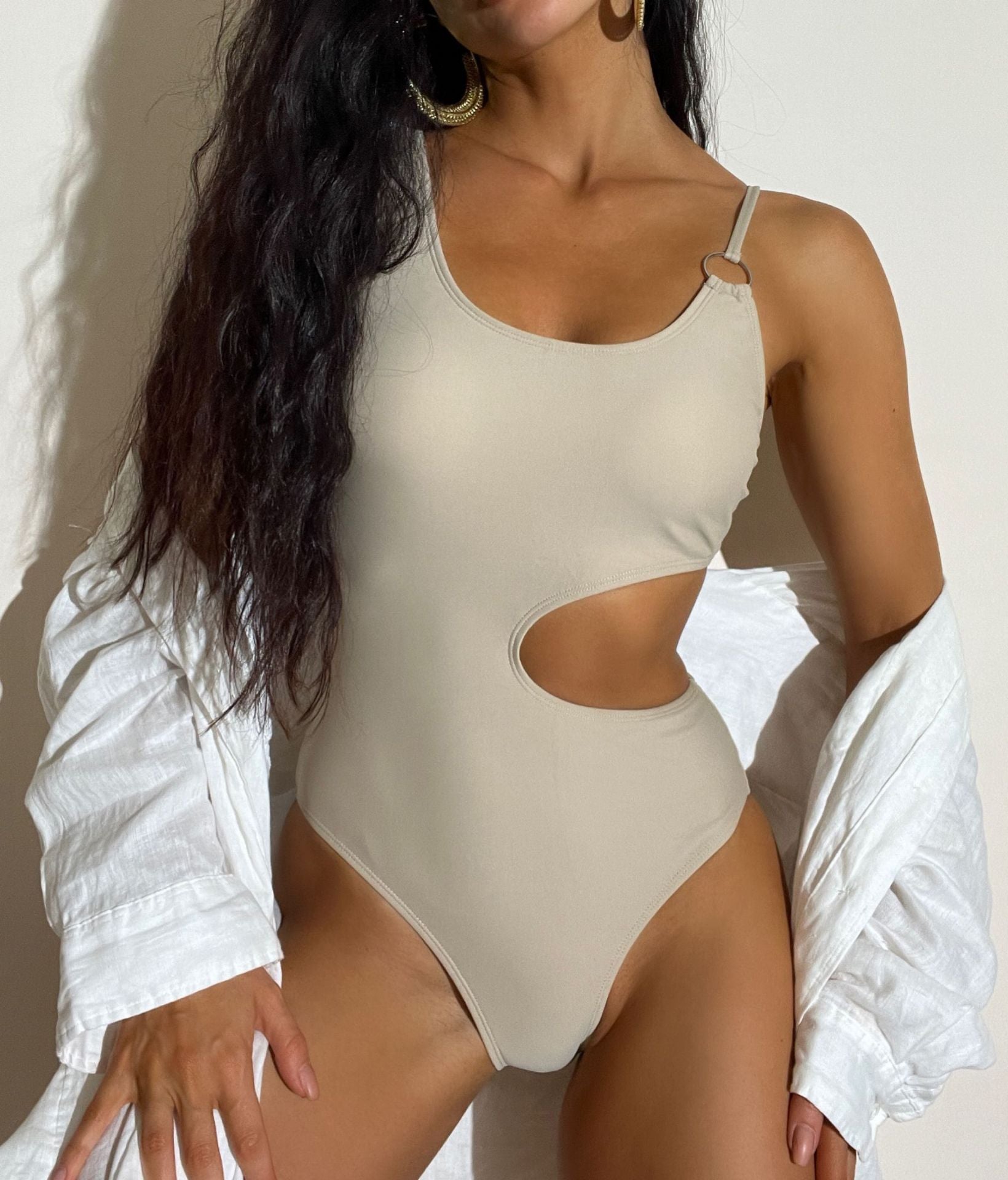 Woman wearing a beige cut-out swimsuit against a neutral background sold at PeachyBeanz.