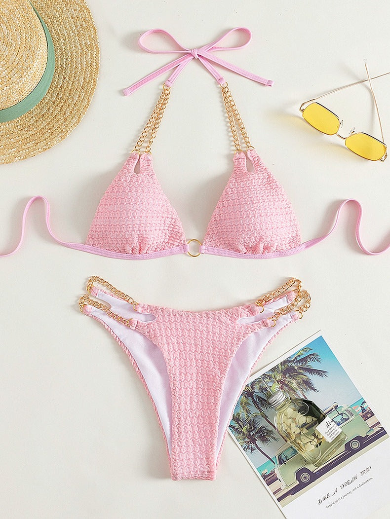 Pink bikini set with gold accents on a white background, accompanied by a straw hat and sunglasses.