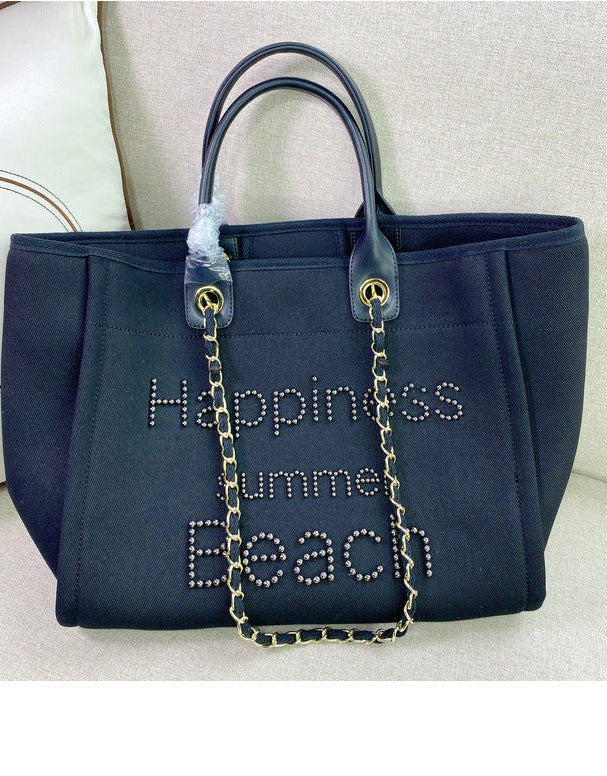 Navy blue handbag with 'Happiness Summer Beach' text and chain detail on a light gray background.