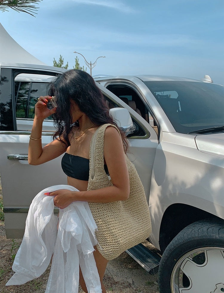 Woman sitting by a white SUV holding a beige bag and a white garment.