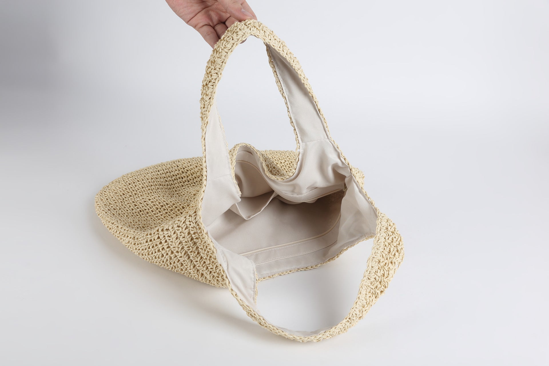 Hand holding a beige woven handbag against a light gray background