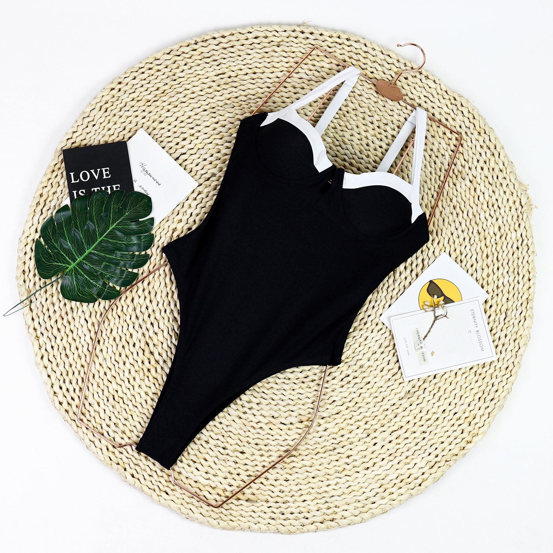 Black swimsuit with white straps on a woven mat with decorative elements