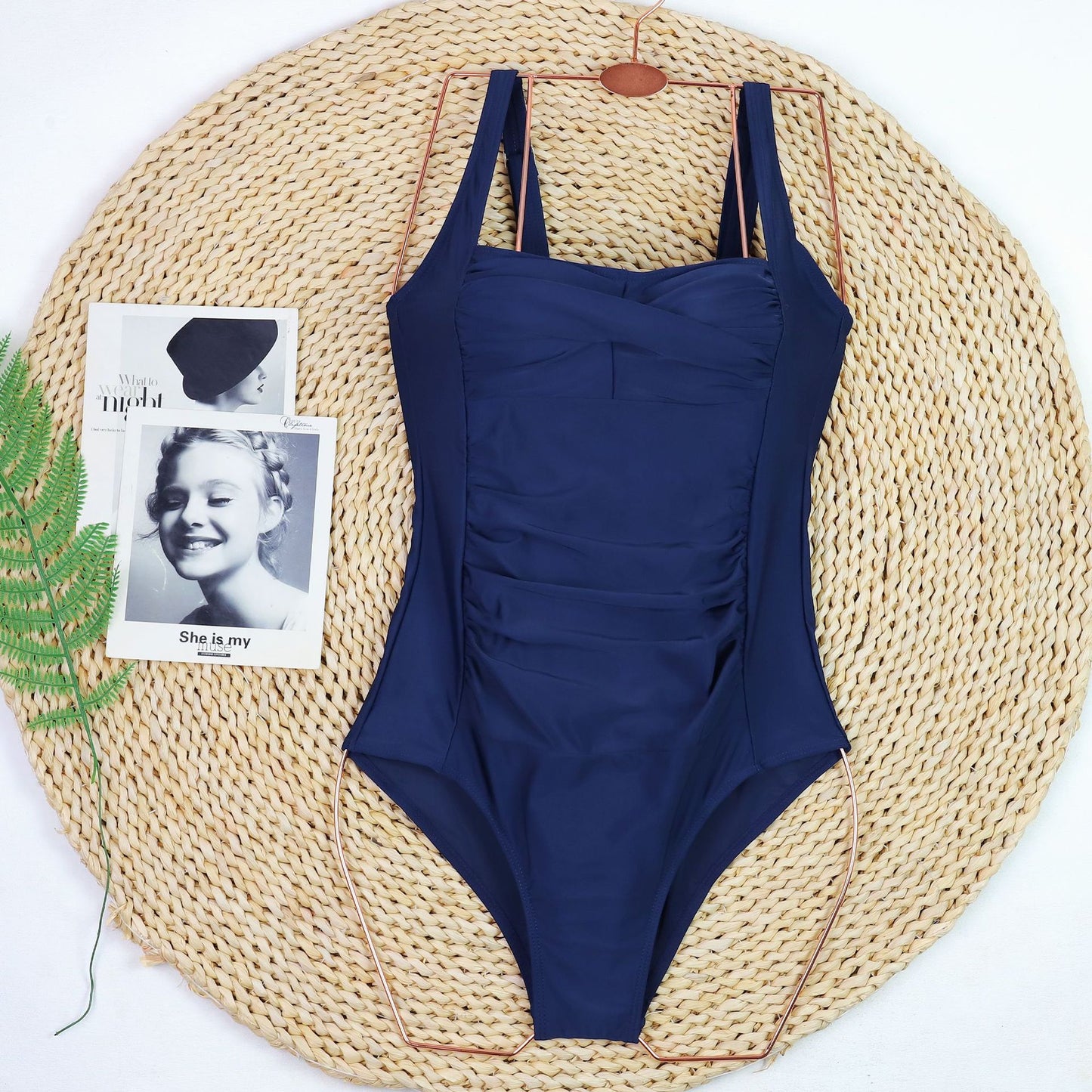 Navy blue swimsuit on a woven mat with a vintage photo and plant leaf. Sold at PeachyBeanz.