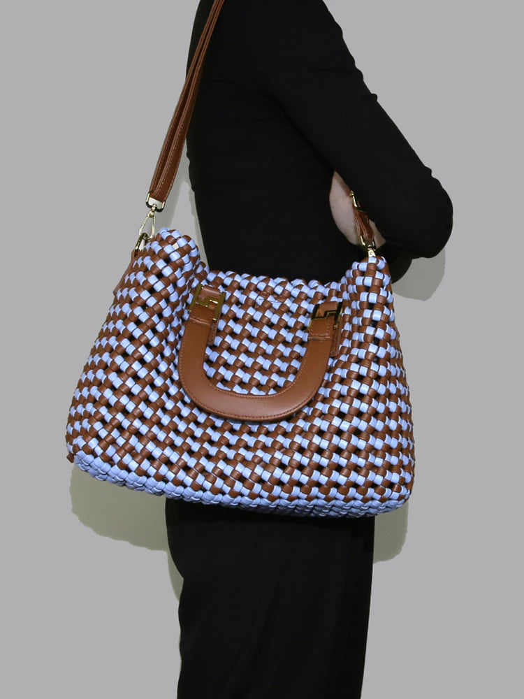 Woven handbag with brown handles held by a person against a plain background