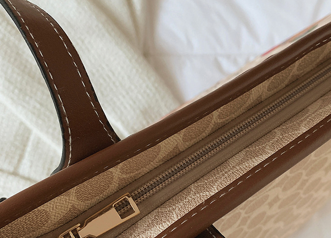 Close-up of a luxury handbag showing the interior zipper compartment with a brown leather trim, beige patterned canvas lining, and gold-tone hardware.