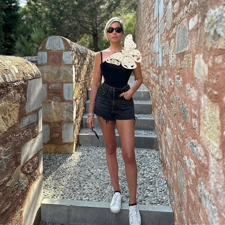 Black two‑piece swimsuit with one‑shoulder top and matching bottoms; padded cups without underwire; solid minimalist design shown on model from front.