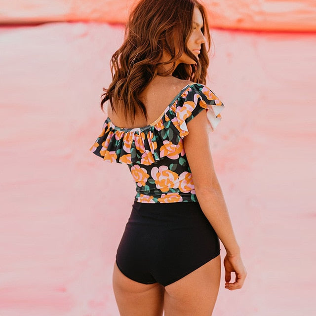 Woman wearing a floral top and black shorts standing against a rocky background