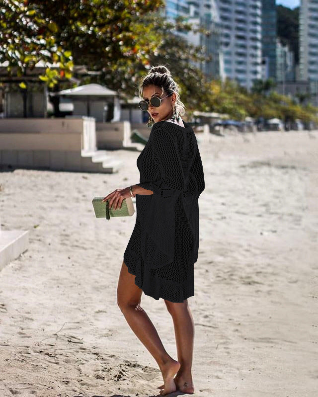 Woman in a black dress standing on a sandy beach with buildings in the background