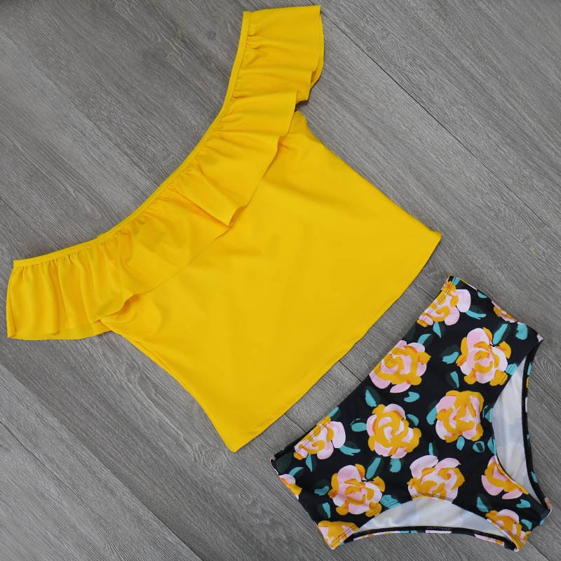 Woman wearing a yellow top and  floral shorts standing against a rocky background