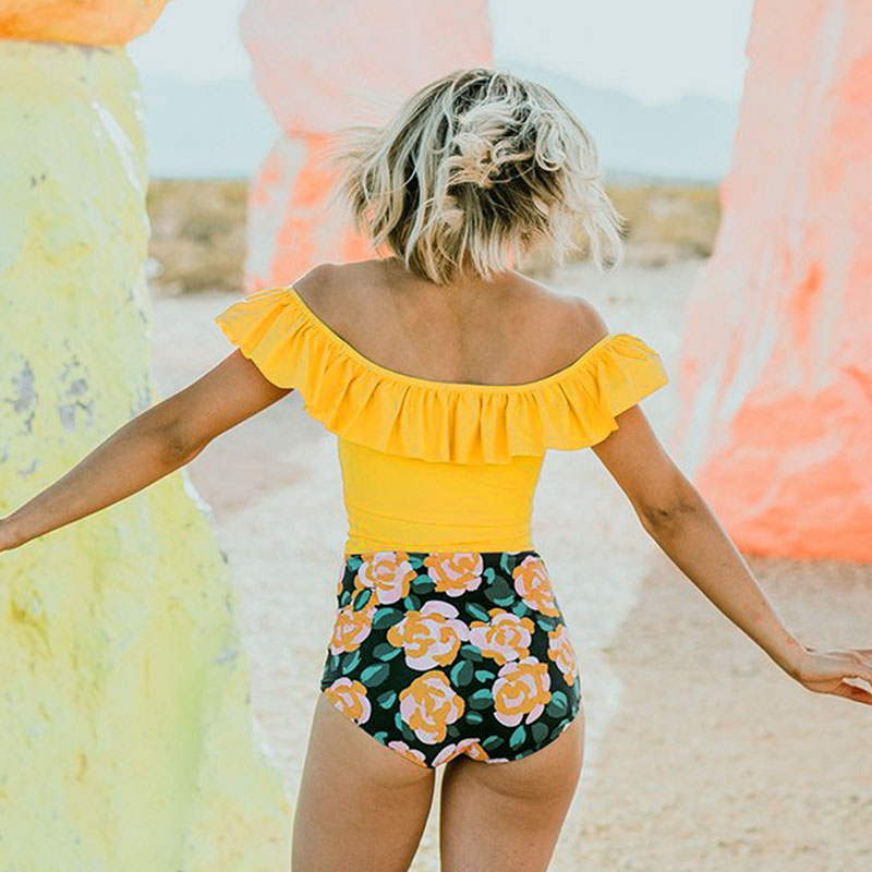 Woman wearing a yellow top and floral shorts standing against a rocky background