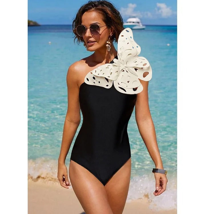 Black two‑piece swimsuit with one‑shoulder top and matching bottoms; padded cups without underwire; solid minimalist design shown on model from front.