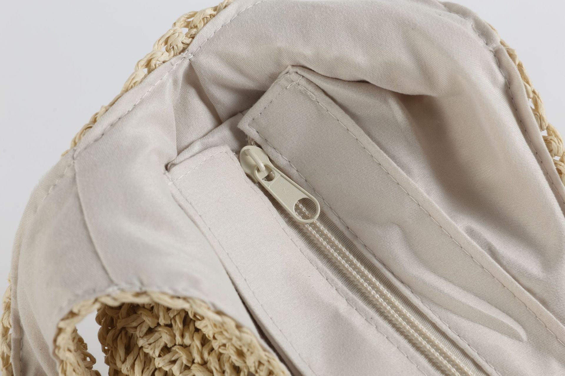 Close-up of a beige fabric bag with a zipper and crochet details on a light gray background