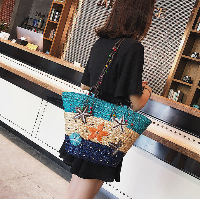 Person holding a colorful woven handbag with decorative elements in an indoor setting.