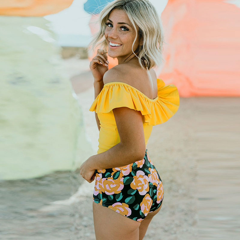 Woman wearing a yellow top and floral shorts standing against a rocky background