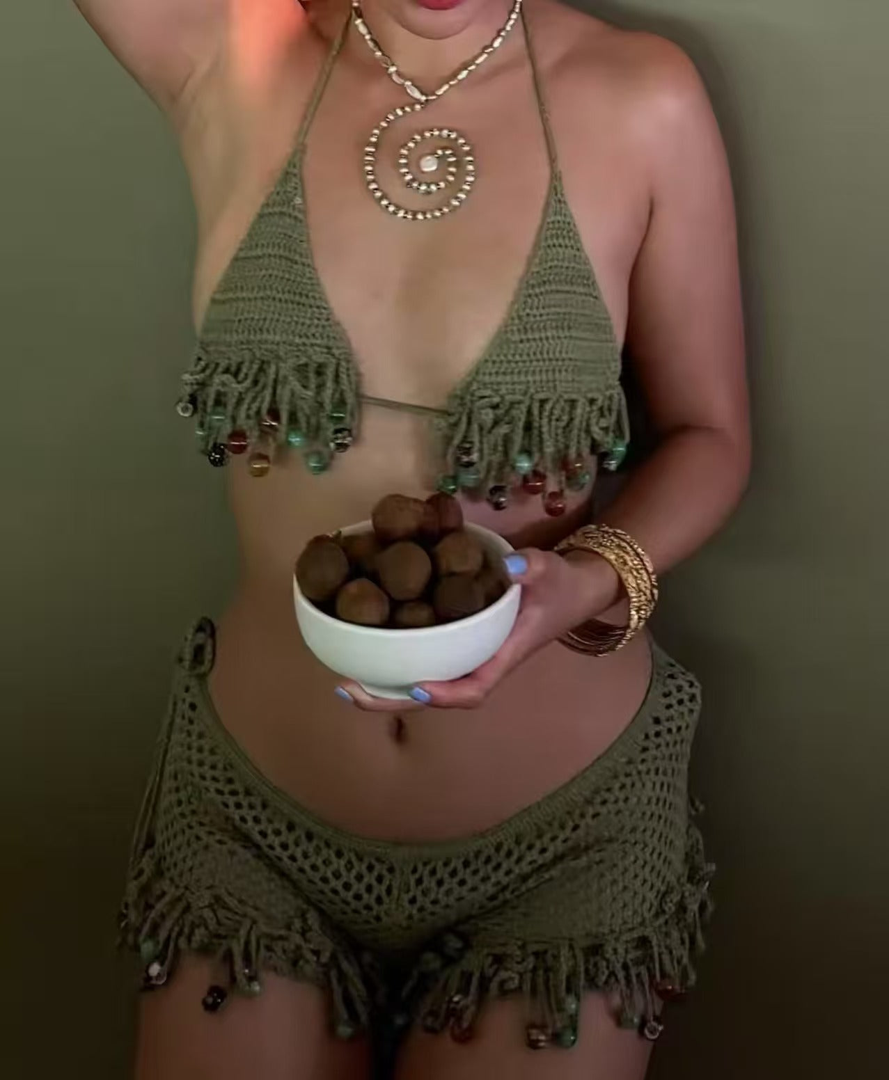 Person wearing a green crochet outfit holding a bowl of dark objects against a plain background